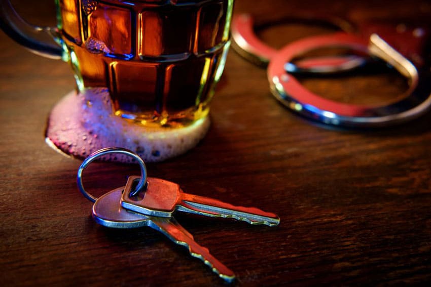 Car keys next to handcuffs and a beer