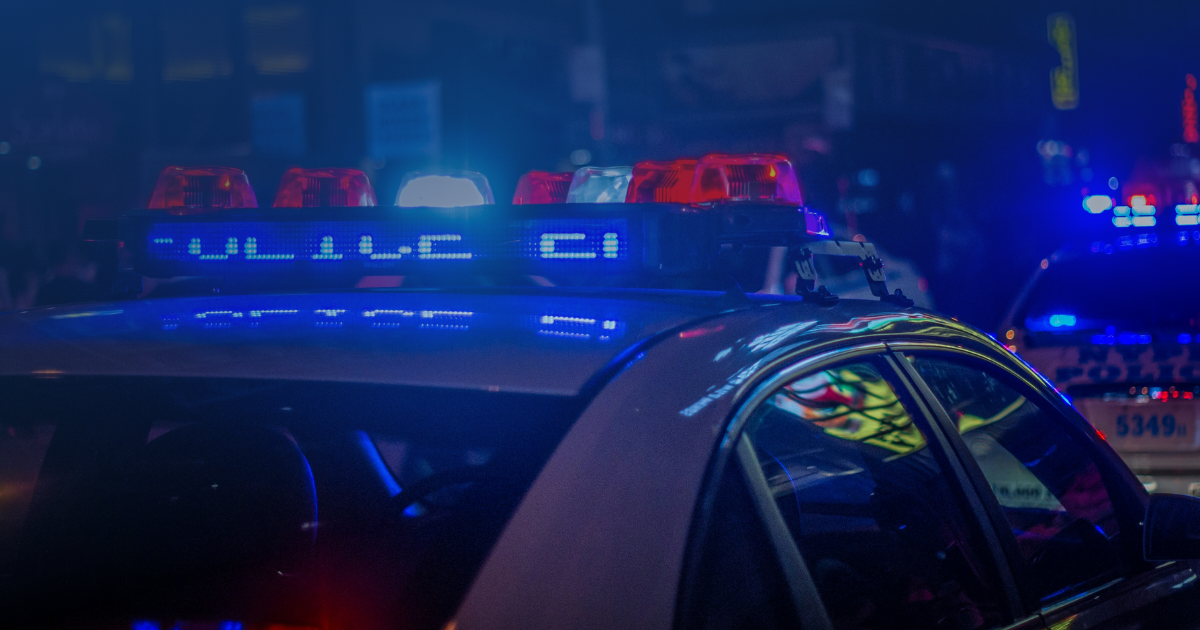 Police car with red and blue emergency lights flashing on a city street at night during a traffic stop